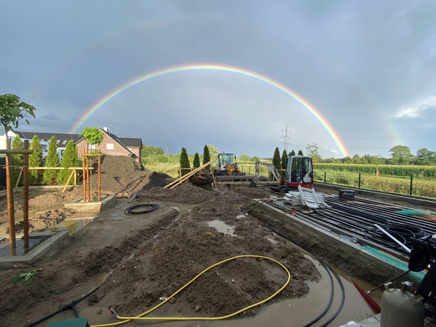 Baustelle mit Erdarbeiten, Radlader und Minibagger unter einem Regenbogen
