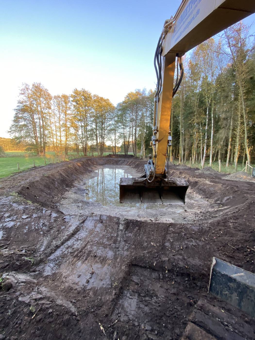 Bagger hebt eine große Grube aus, am Boden steht Wasser