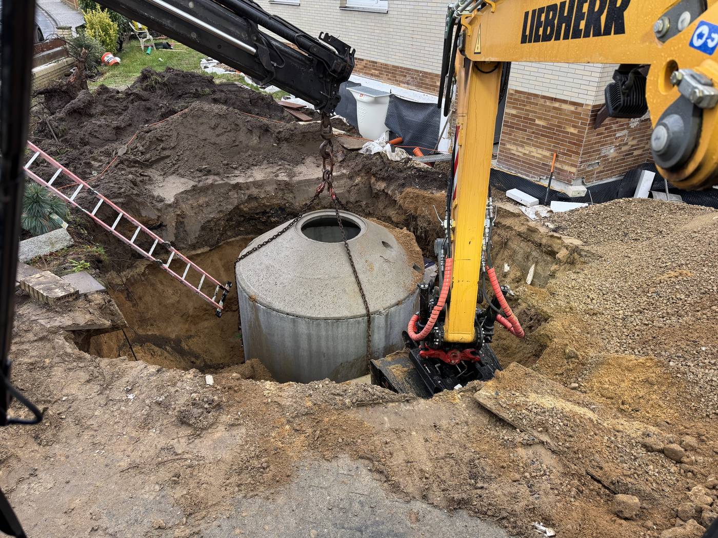 Bagger setzt einen Betonschacht in die Baugrube am Haus